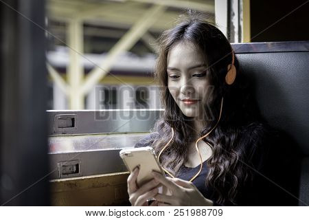 Asian Woman Traveler Has Listening Music With Phone And Orange Headphone Inside The Train At Hua Lam