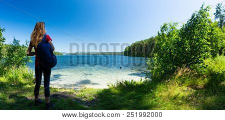 Hiker stands on the green coast of a crystal clear lake. Lake of Turgoyak, Russia