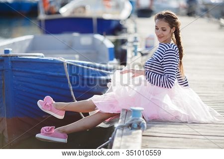 Happy Young Womanl With A Long Braid Happy Laughing While Sitting Outdoor With Boats On Background. 