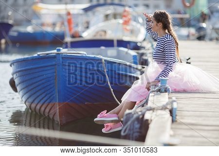 Happy Young Womanl With A Long Braid Happy Laughing While Sitting Outdoor With Boats On Background. 
