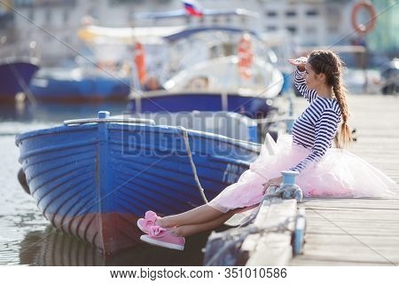 Happy Young Womanl With A Long Braid Happy Laughing While Sitting Outdoor With Boats On Background. 