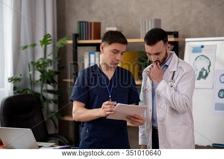 Two Young Male Doctors Looking Thoughtful While Discussing Medical Case In The Staffroom