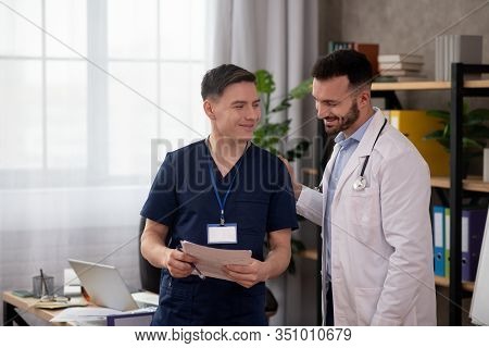 Two Young Male Doctors Discussing Medical Case In The Staffroom