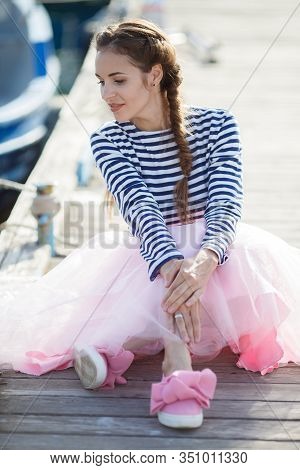 Happy Young Womanl With A Long Braid Happy Laughing While Sitting Outdoor With Boats On Background. 