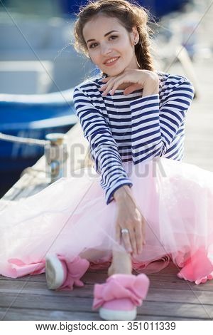 Happy Young Womanl With A Long Braid Happy Laughing While Sitting Outdoor With Boats On Background. 