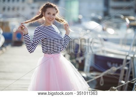 Happy Young Womanl With A Long Braid Happy Laughing While Sitting Outdoor With Boats On Background. 