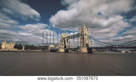 Tower Bridge over river Thames with sailing boats ships and London Tower Fortress lit by sunlight under blue sky. Soft clouds fast motion in blue sky. Travel recreation concept.