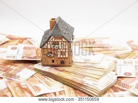 A Ceramic House Stands On A Pile Of Five Thousand Ruble Bills. Symbol Of Success, Improvement Of Liv