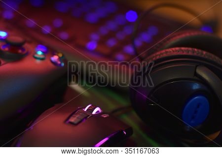 Modern Gamepad And Gaming Mouse Lies With Keyboard And Headphones On Table In Dark Playroom Scene. E