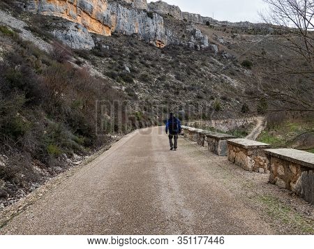 Man With A Blue Backpack Walking In The Middle Of A Sandy Path Surrounded By Rock Formations On The 