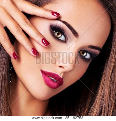 Closeup portrait of beautiful seductive woman with dark brown eye makeup and bright red lips and nails