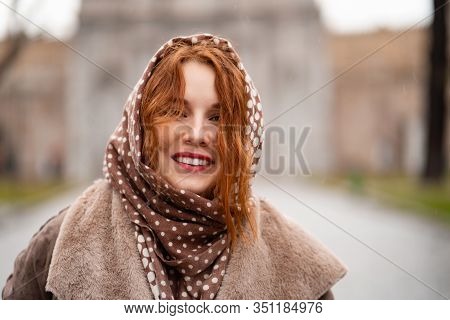 Beautiful Red-haired Girl With Red Lips In A Scarf Smiling In The Rain