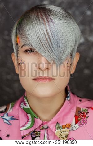 Portrait Of A Young Beautiful Girl In A Pink Shirt On A Gray Background With Dyed Hair. Short Haircu