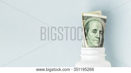Money Bills In White Pill Bottle On Blue Background. Medical Concept With Copyspace