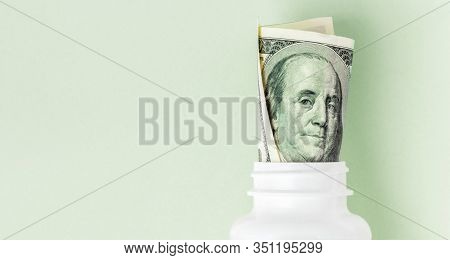Roll Of Money Bills In White Pill Bottle On Pink Background With Copy Space. Medicine Flat Lay