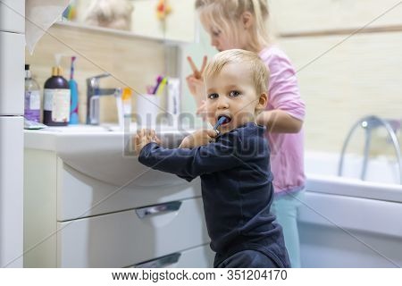 Two Cute Adorable Blond Caucasian Siblings Washing Face And Cleaning Tooth With Toothbrush At Bathro
