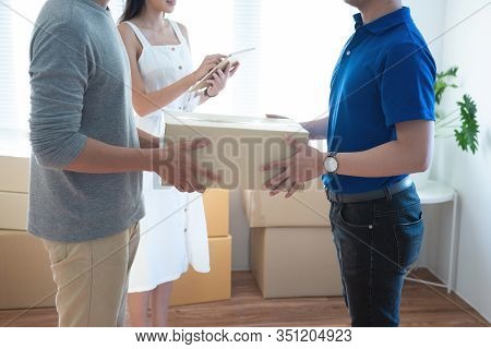 Delivery Service Worker In Uniform Delivering Parcels To Happy Asian Couple. Woman With Tablet Signi