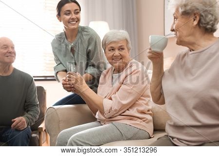 Young Woman Taking Care Of Elderly People In Living Room