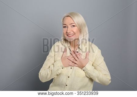 Happy Woman Holding Hands Near Heart On Grey Background
