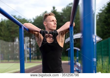 A Muscular Man Stands Leaning On Parallel Bars, With A Bare Torso.