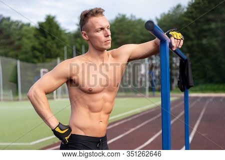 A Muscular Man Stands Near Parallel Bars, With A Bare Torso.