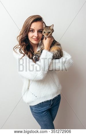 Girl In A White Sweater Hugs A Gray Cat On A White Background.