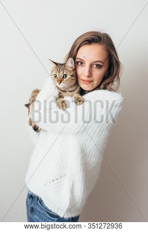 Girl In A White Sweater Hugs A Gray Cat On A White Background.