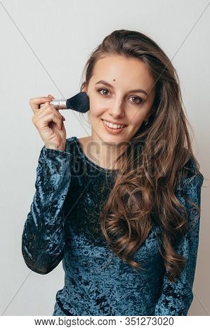 Beautiful Young Woman In Shiny Green Dress Applying Powder With A Brush To The Face.