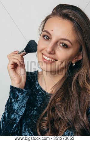 Beautiful Young Woman In Shiny Green Dress Applying Powder With A Brush To The Face.