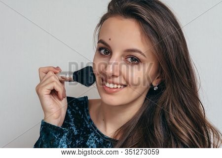 Beautiful Young Woman In Shiny Green Dress Applying Powder With A Brush To The Face.