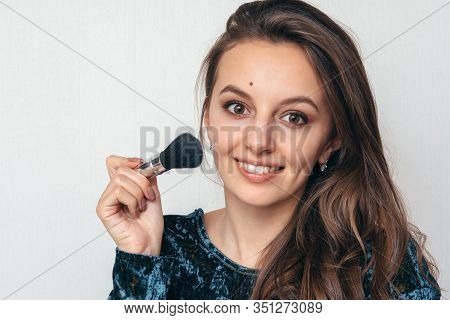 Beautiful Young Woman In Shiny Green Dress Applying Powder With A Brush To The Face.