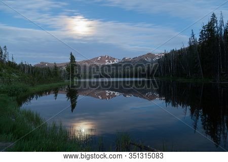 The Full Moon Over Top Notch Peak Is Reflecting Light Onto Sylvian Lake In Yellowstone National Park