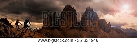 Cycling outdoor adventure in Dolomites. Cycling woman and man  on electric mountain bikes in Dolomites landscape. Couple cycling MTB enduro trail track. Outdoor sport activity.
