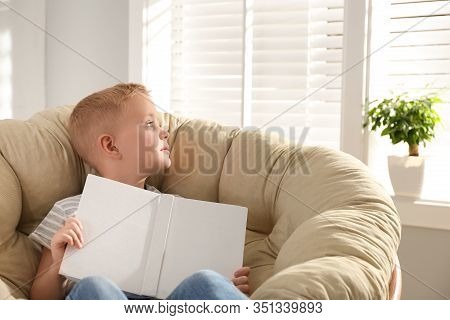 Cute Little Boy With Book In Papasan Chair At Home