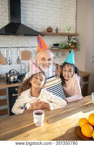 Two Dark-skinned Girls In Bday Hats Feeling Happy With Their Granddad