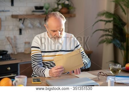 Bearded Grey-haired Man Sitting At The Table With A Newspapaer In His Hands