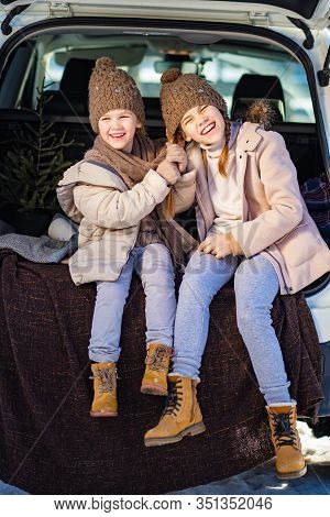 Two Sisters Sitting At The Top In The Trunk Of A Car And  Pull The Tail. Outdoors In The Winter.
