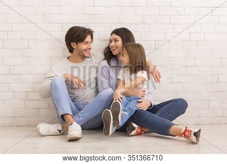 Casual Family. Portrait Of Cheerful Mom, Dad And Their Little Daughter Ebracing Together And Sitting