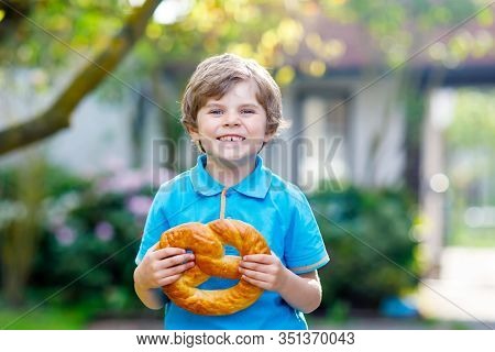 Adorable Little Kid Boy Eating Huge Big Bavarian German Pretzel. Happy Blond Child Enjoying Tasteful
