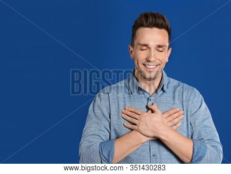 Handsome Grateful Man With Hands On Chest Against Blue Background