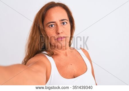 Middle age mature woman taking a selfie photo using smartphone over isolated background with a confident expression on smart face thinking serious