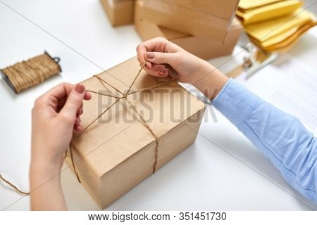 delivery, mail service, people and shipment concept - close up of female hands packing eco parcel box and tying rope at post office