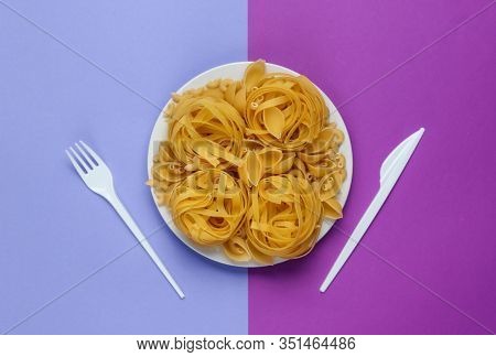 Different Types Of Raw Italian Pasta In A Plate, Fork And Knife On Purple Background. Top View.