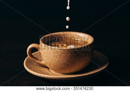 Milk Is Pouring Into A Cup Of Coffee On A Black Background.