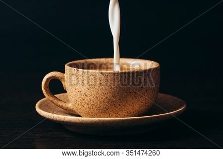 Milk Is Pouring Into A Cup Of Coffee On A Black Background.