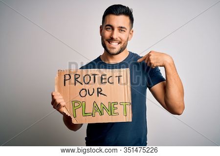 Young handsome activist man protesting for the enviroment hoding cardboard with surprise face pointing finger to himself
