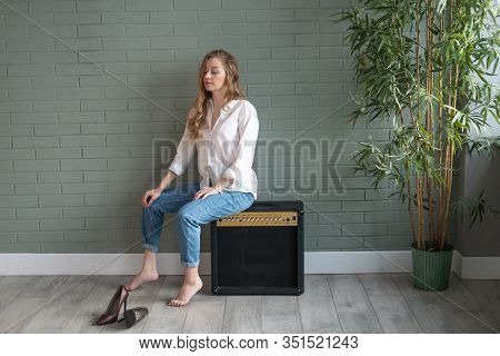 Young Beautiful Woman Sitting On Subwoofer With Bare Feet Next To Green Plant