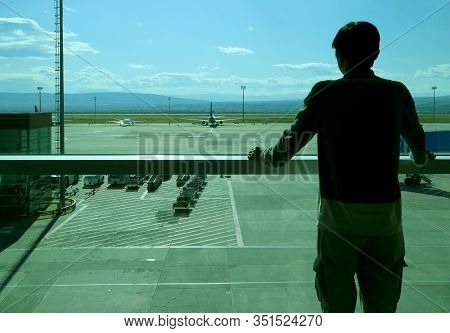 Silhouette Of A Man At The Airport's Boarding Hall Looking At The Airplane On Runway