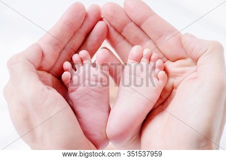 Father holds newborn baby's feets. Tiny legs in father's strong hand on white background. Healthcare, pediatrics.