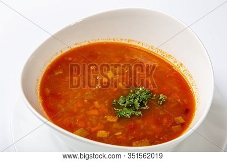Beef Goulash Soup With Tongue. A White Oval Plate With Red Soup Stands On A White Background.